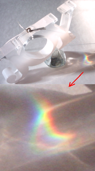 Picture of a clear plastic object that spells joy with sunlight striking it. The word is raised up by a small glass object so the proper angle could be made to create rainbow colors on white cardboard. The rainbow colors are enlarged in another image attached to this picture.